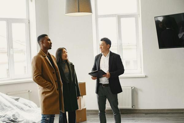 A man with a clipboard standing in an empty, modern living room with a young couple